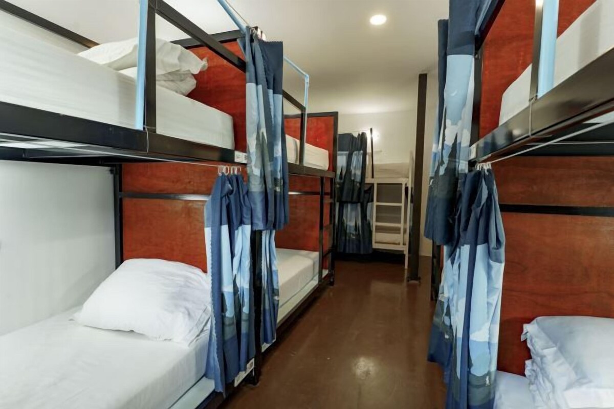 A narrow corridor with bunk beds on either side, a wooden floor, and a door at the end.