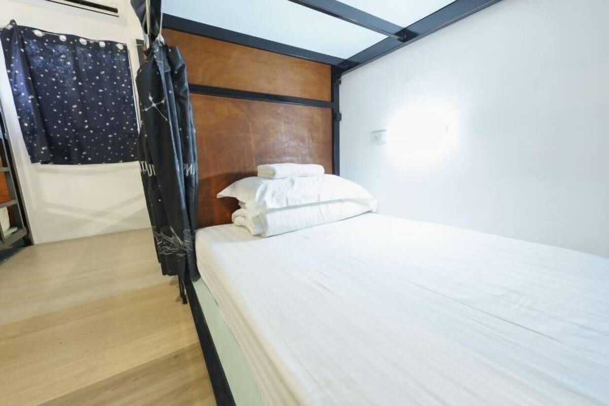 Un lit simple avec une literie blanche, une tête de lit en bois et un rideau foncé.
