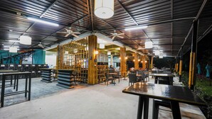 An indoor dining area with high ceilings, exposed beams, and a mix of indoor and outdoor seating. - Green Gen Hotel Phuket (Ratsada)
