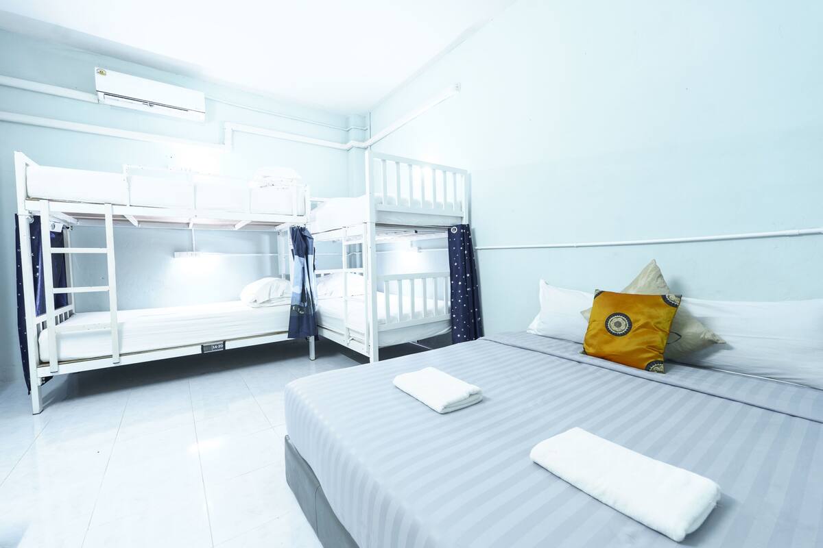 Une chambre avec des lits superposés et un lit simple, un climatiseur blanc et une fenêtre avec des rideaux.
