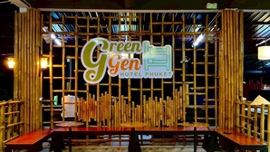 A hotel interior with a bamboo partition, a sign reading "Green Gen Hotel Phuket", and a seating area with tables and benches. - Green Gen Hotel Phuket (Ratsada)
