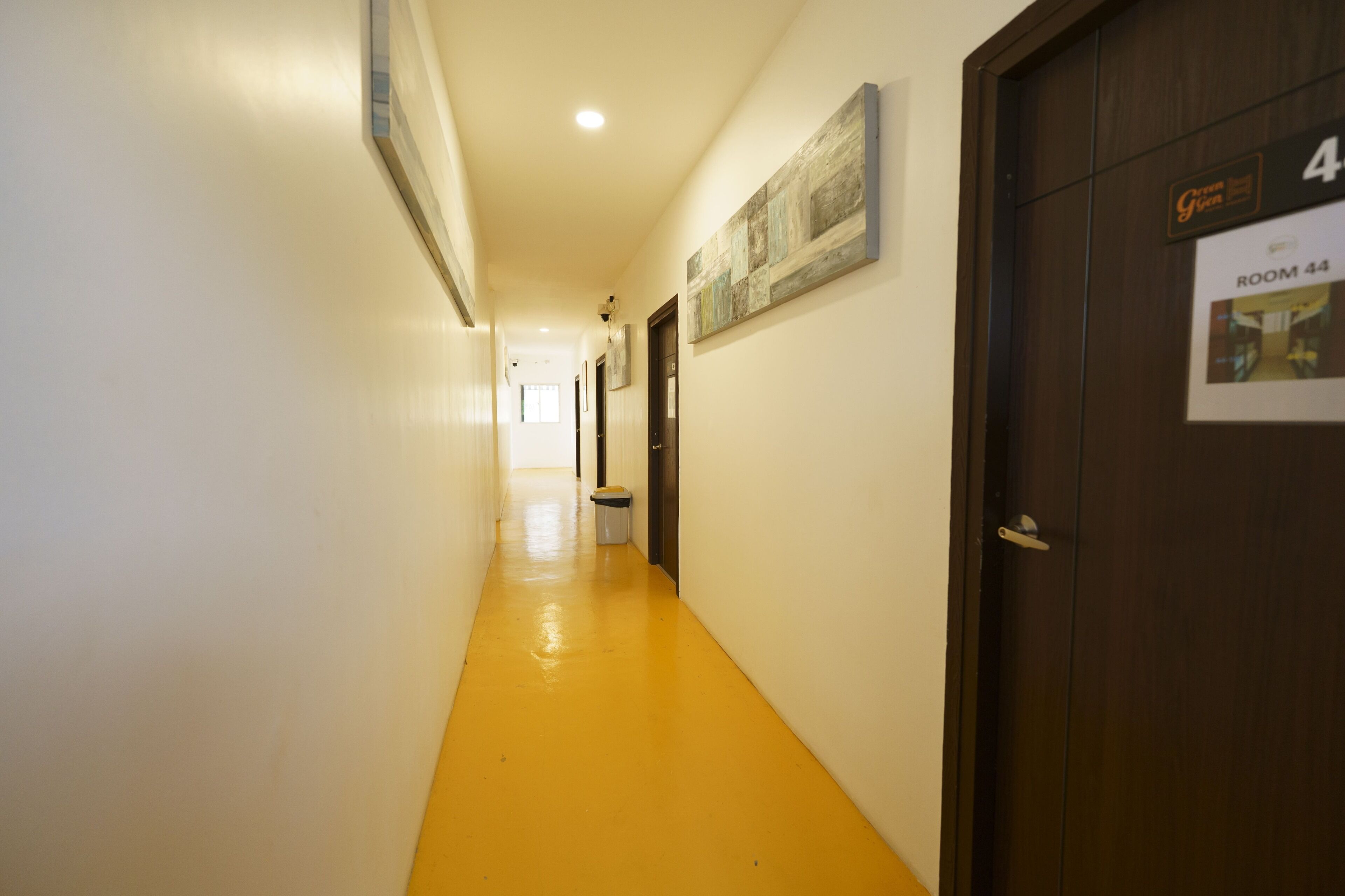 Un couloir d’hôtel avec un sol jaune, une porte portant l’inscription « CHAMBRE 44 » et une enseigne au-dessus de la porte.