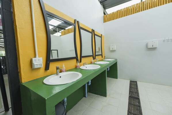 Tres lavamanos en línea con espejos, encimera verde y pared amarilla.