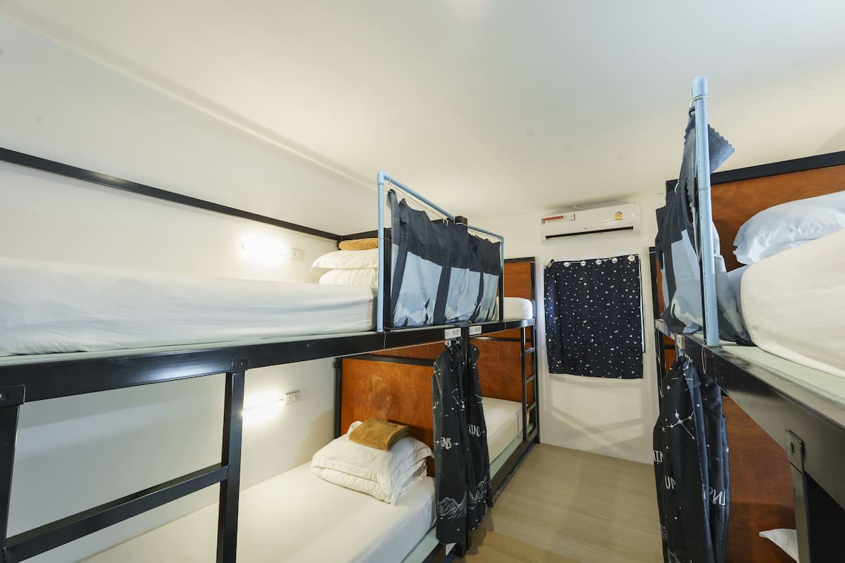Une chambre avec un lit superposé doté d’une tête de lit en bois, une fenêtre ornée d’un rideau à motifs d’étoiles et un climatiseur fixé au mur.