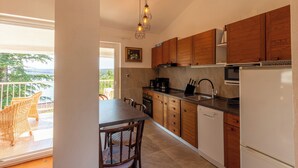 A kitchen with wooden cabinets, a dishwasher, and a dining area with wicker chairs. - Apartment Azzuro Bay 2 (Jadranovo)