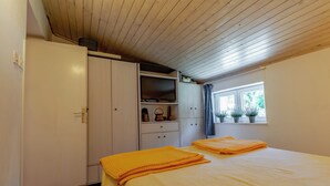 A bedroom with a bed, a wardrobe, a shelf with items, and a window with plants. - Apartment Azzuro Bay 2 (Jadranovo)