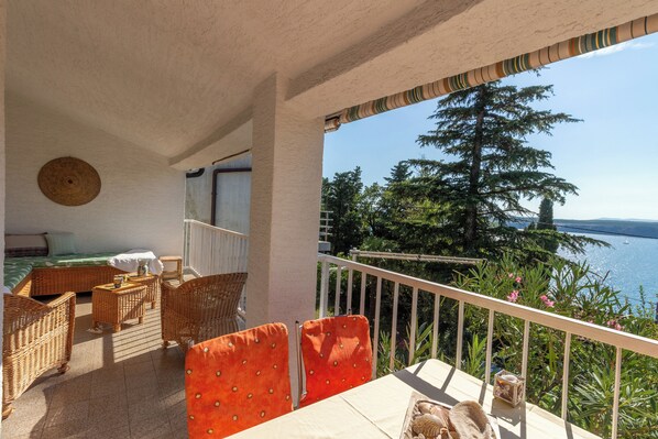 Un balcon avec des meubles en osier, une vue sur la mer et un lit recouvert d’une couverture verte.