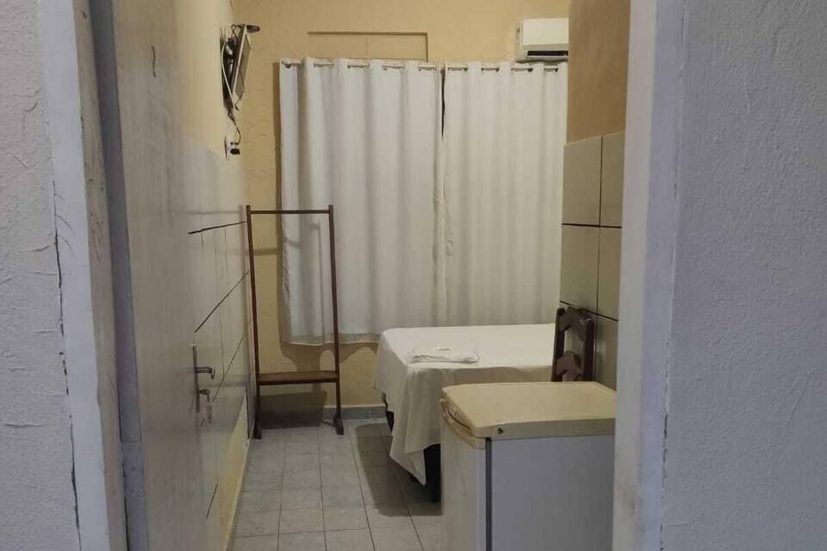A small, narrow room with a bed, a small table, and a shower area.