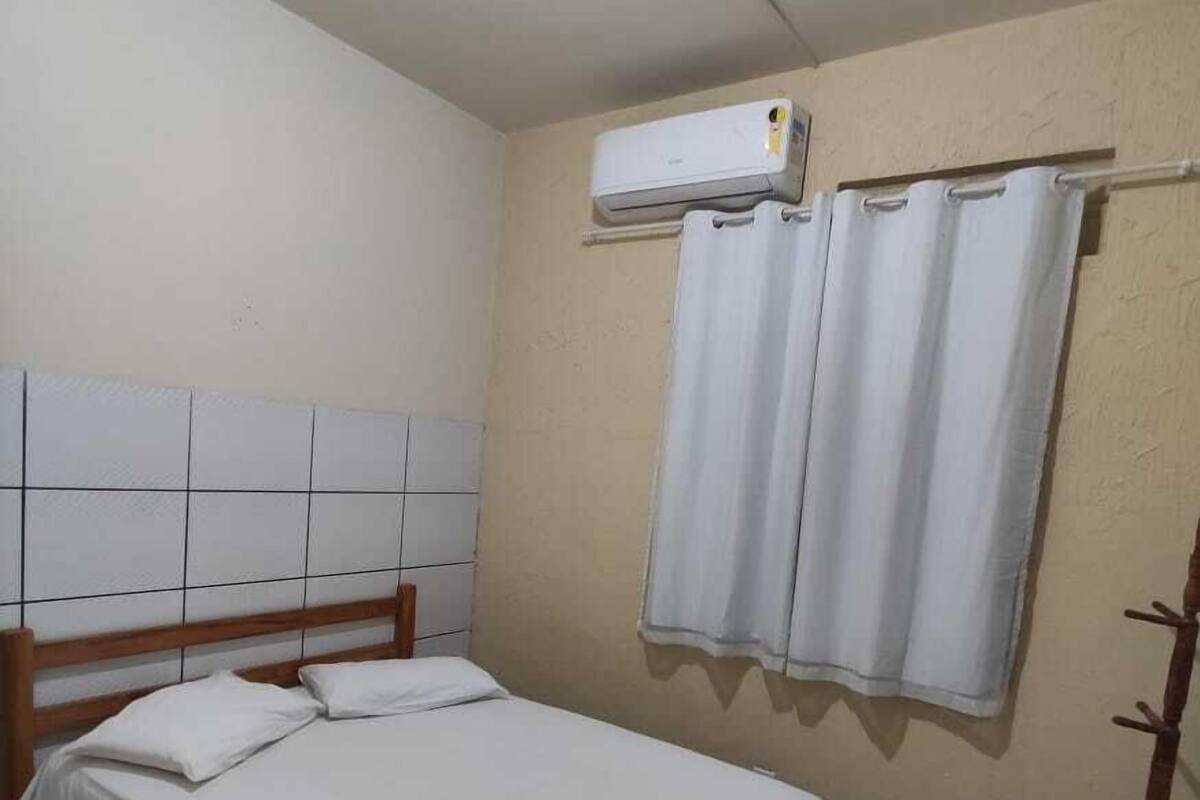 A single bed with a wooden headboard, a white bedspread, and a wall-mounted air conditioner.