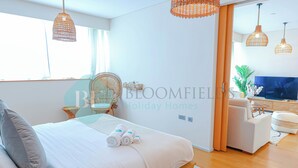 Une chambre moderne avec un grand lit, deux lampes suspendues en osier, une télévision et un canapé.