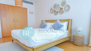 Une chambre avec un lit en bois, une literie blanche et un pouf en osier.