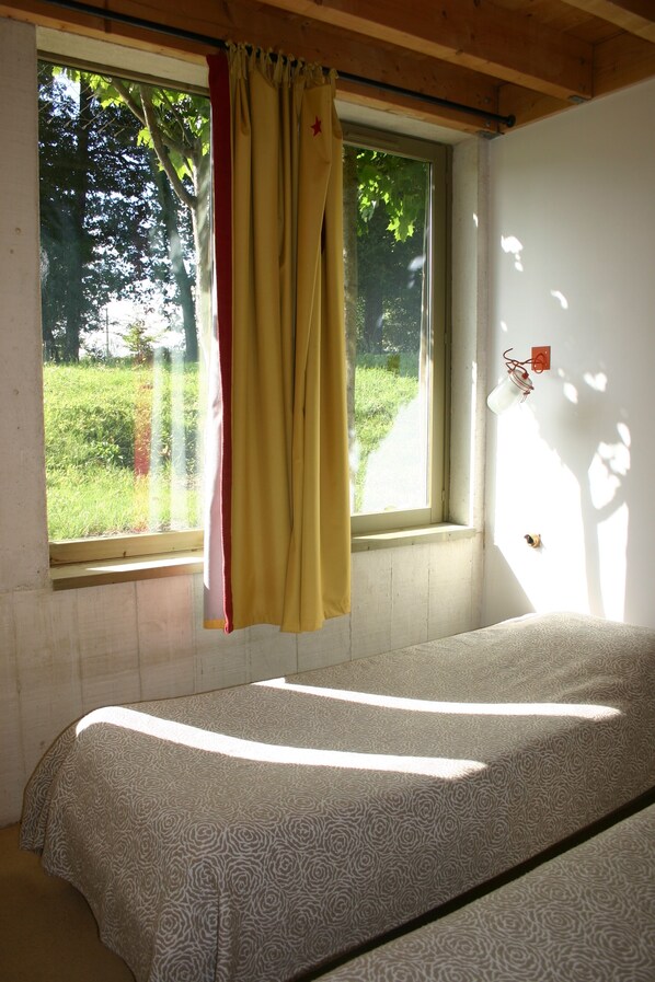A single bed in a room with a window, a curtain, and a wall-mounted light fixture.