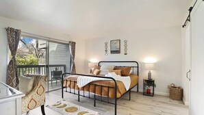 Een slaapkamer met een bed, een stoel, een klein tafeltje en een raam met gordijnen.
