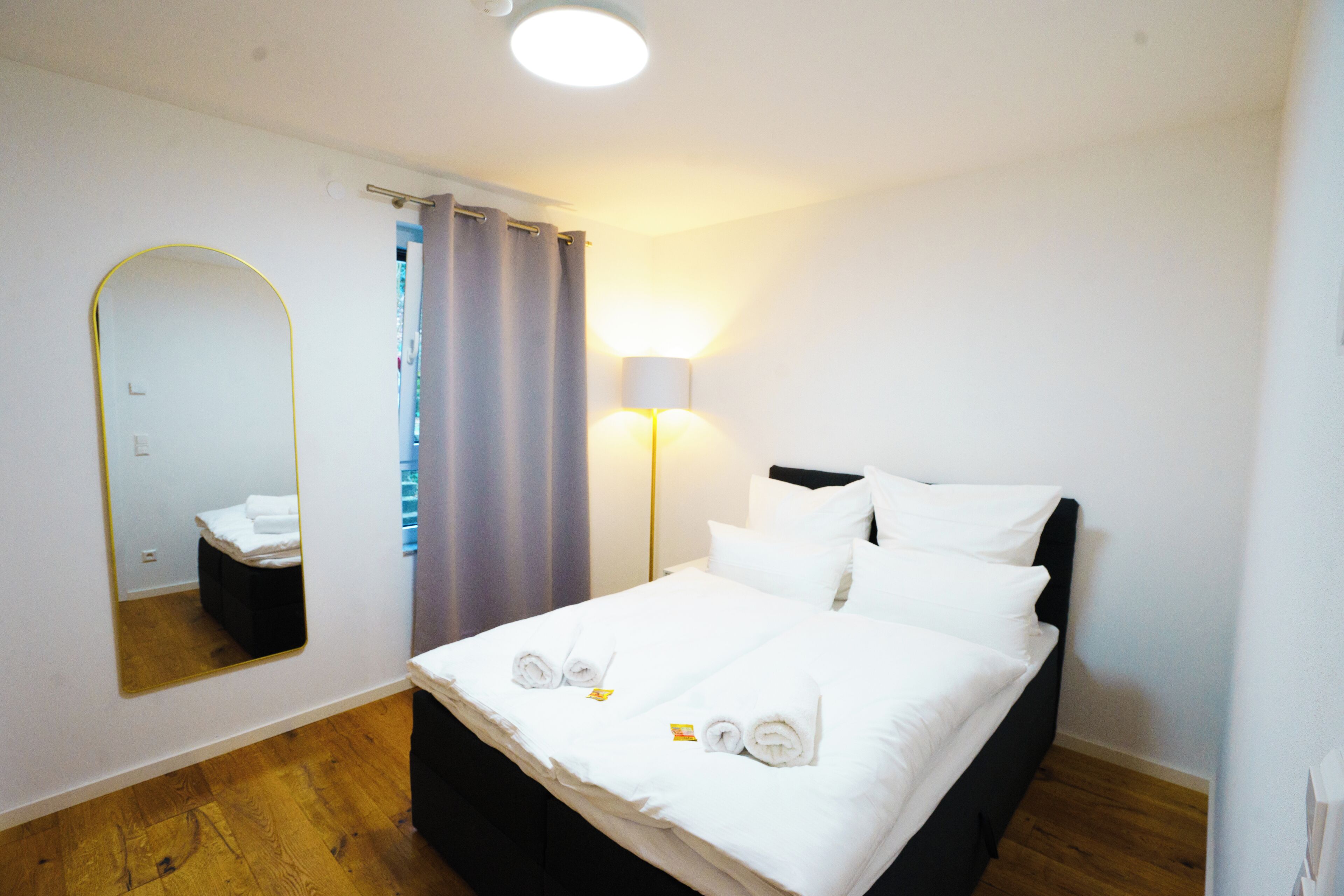 Ett hotellrum med en säng, en spegel, en lampa och ett trägolv.