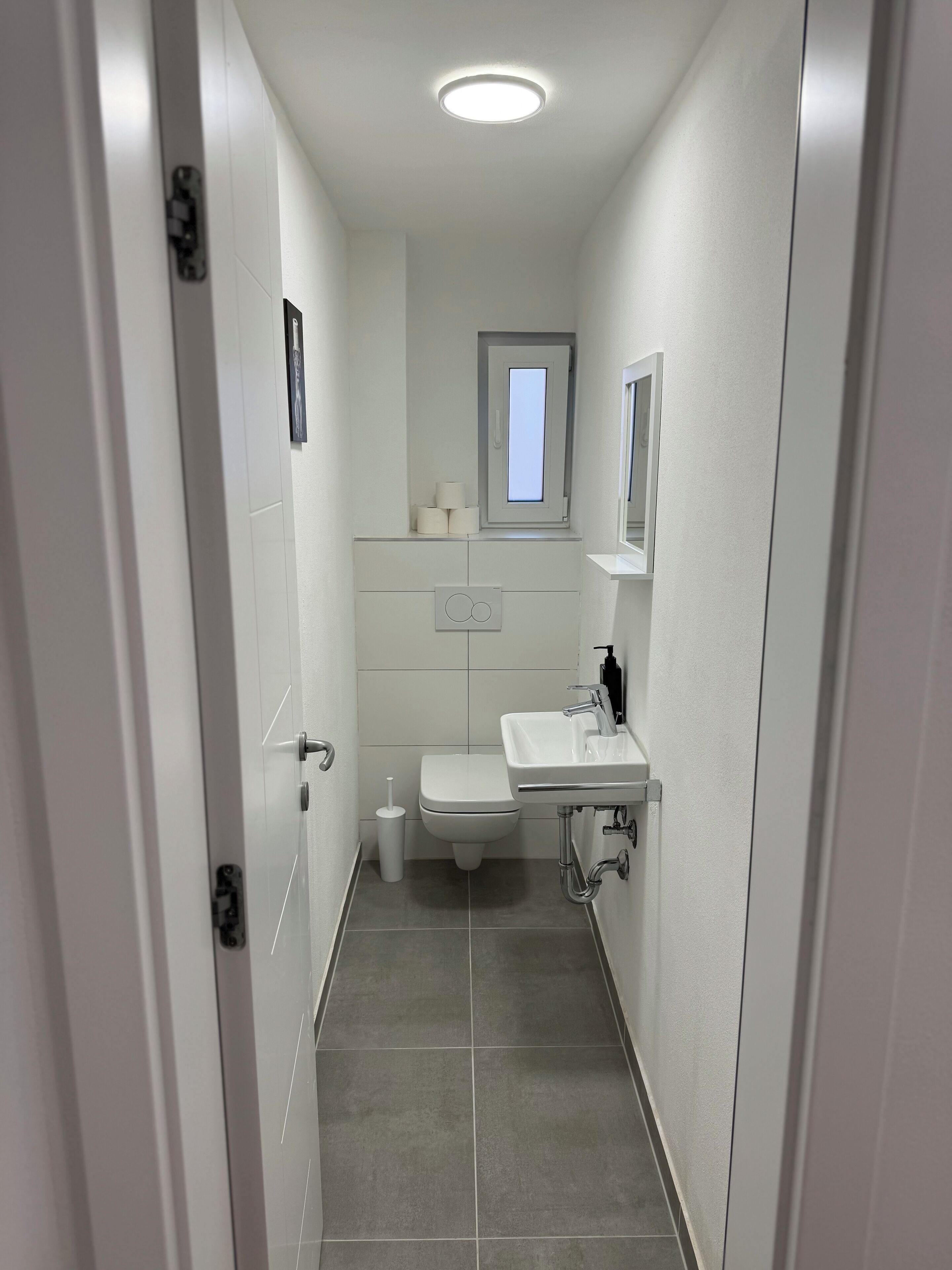 Un baño estrecho con inodoro, lavamanos y ventana.