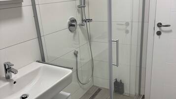 Un baño moderno con ducha acristalada, lavabo blanco y retrete.