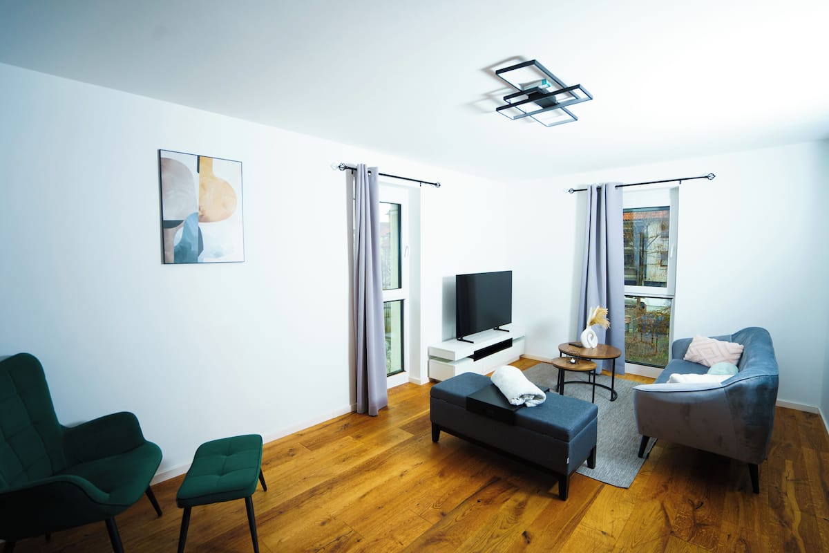 Un salon moderne avec un canapé, deux fauteuils, un téléviseur et une petite table.