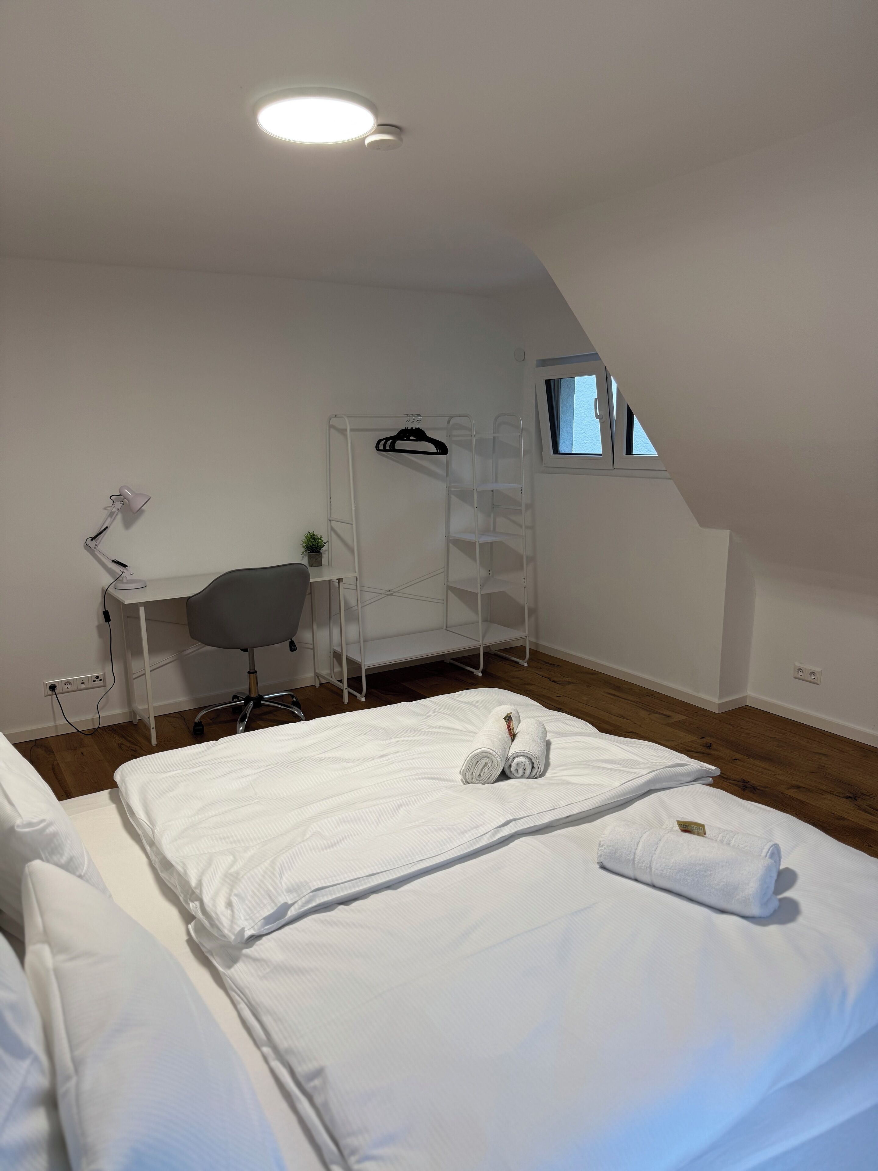 A bedroom with a bunk bed, a desk with a chair, a hanging rack, and a window.