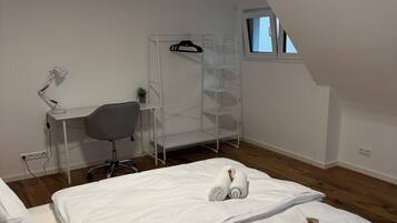 A bedroom with a bunk bed, a desk with a chair, a hanging rack, and a window.