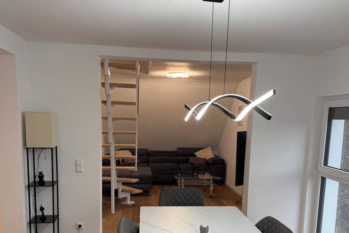 Un espace de vie moderne avec une table à manger en marbre blanc, des chaises en cuir noir, un canapé noir et un escalier menant à un niveau supérieur.