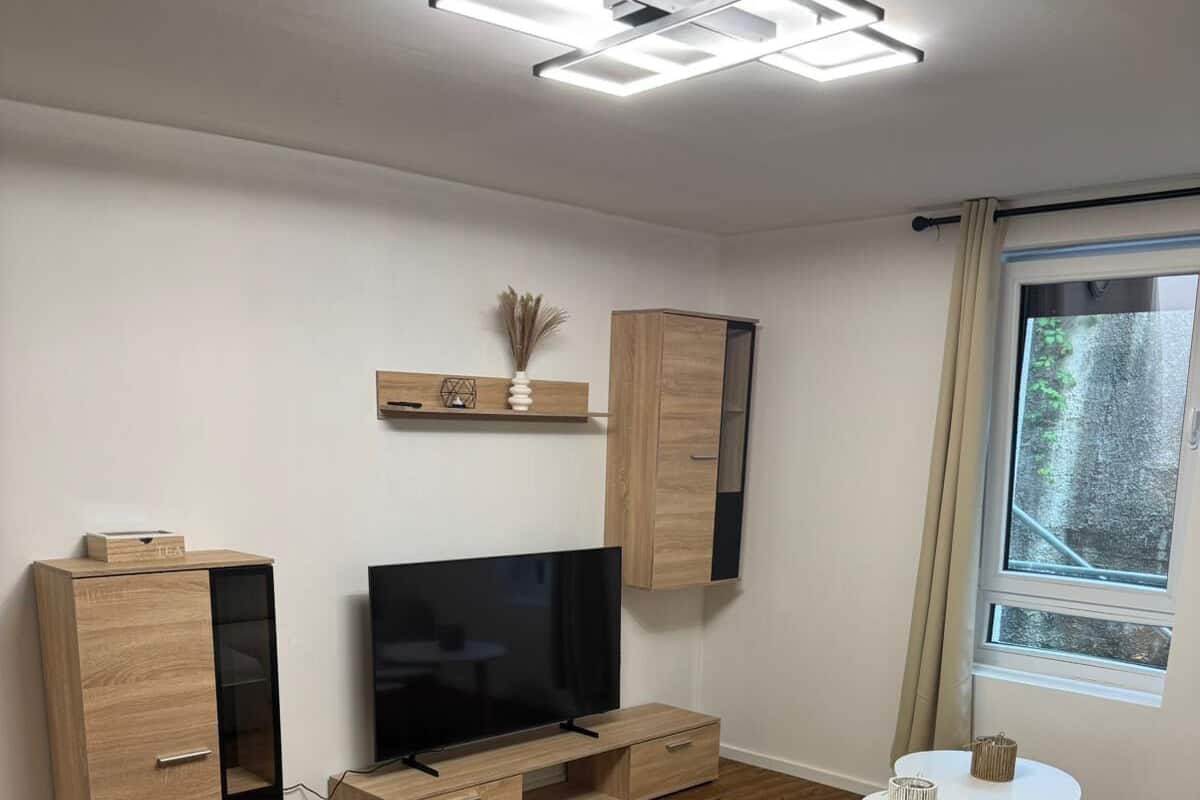 Un salon moderne avec un téléviseur, un meuble en bois et un coin repas comprenant une table ronde et des chaises.