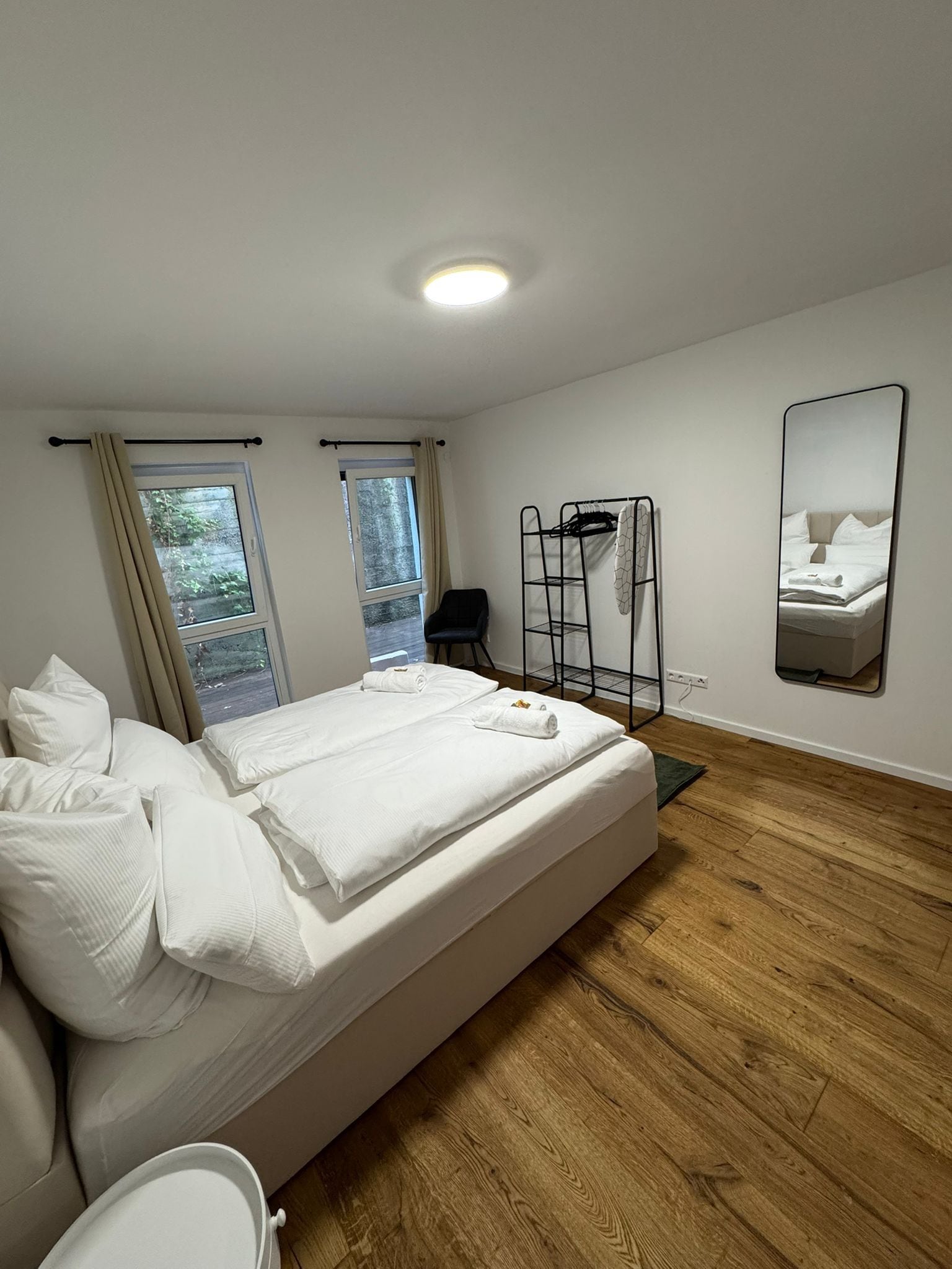 A hotel room with a bed, a chair, a mirror, and a window.