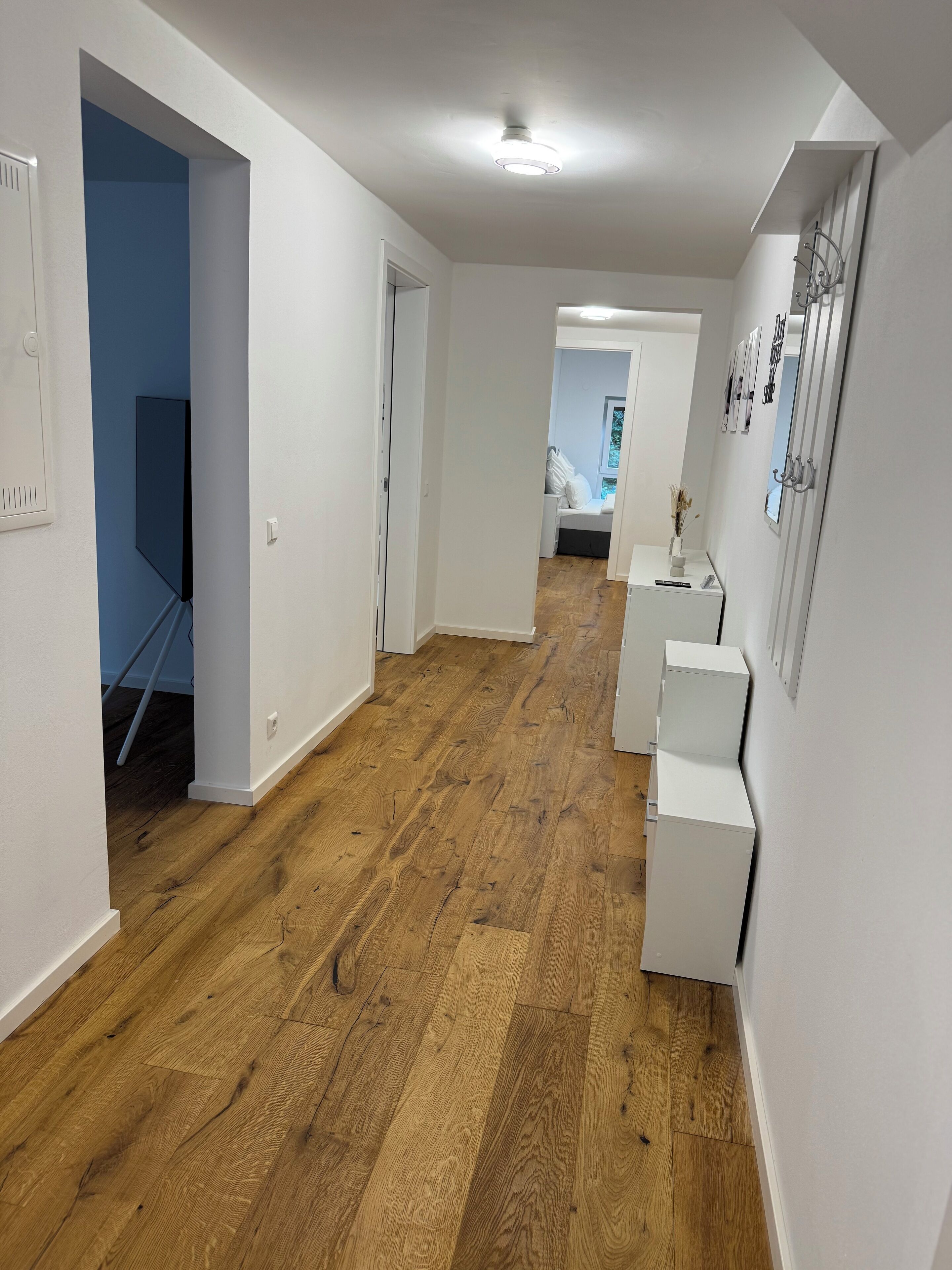 A hallway with wooden flooring, white walls, and a door leading to a bedroom.