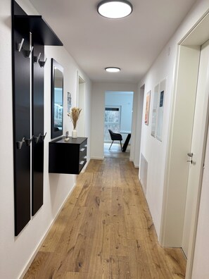 A hallway with a wooden floor, black cabinets, a mirror, and a vase with dried flowers. - KC Hostings - Prestige Apartments (Reutlingen)