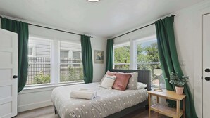 Ein Schlafzimmer mit einem Bett, grünen Vorhängen, einem Nachttisch mit einer Lampe und einem Fenster mit Jalousien.