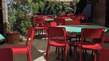 An outdoor patio with red chairs and tables, surrounded by potted plants and a brick wall.