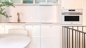 Una cocina compacta con un lavamanos, una estufa y armarios. En primer plano, hay una mesa pequeña y una silla.