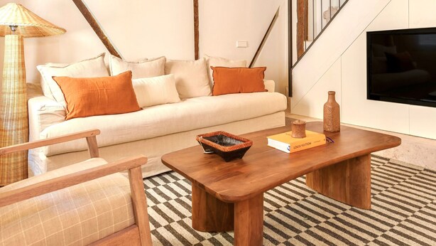 Una sala de estar con sofá, una mesa de centro de madera, una lámpara de pie de mimbre y un tapiz estampado.