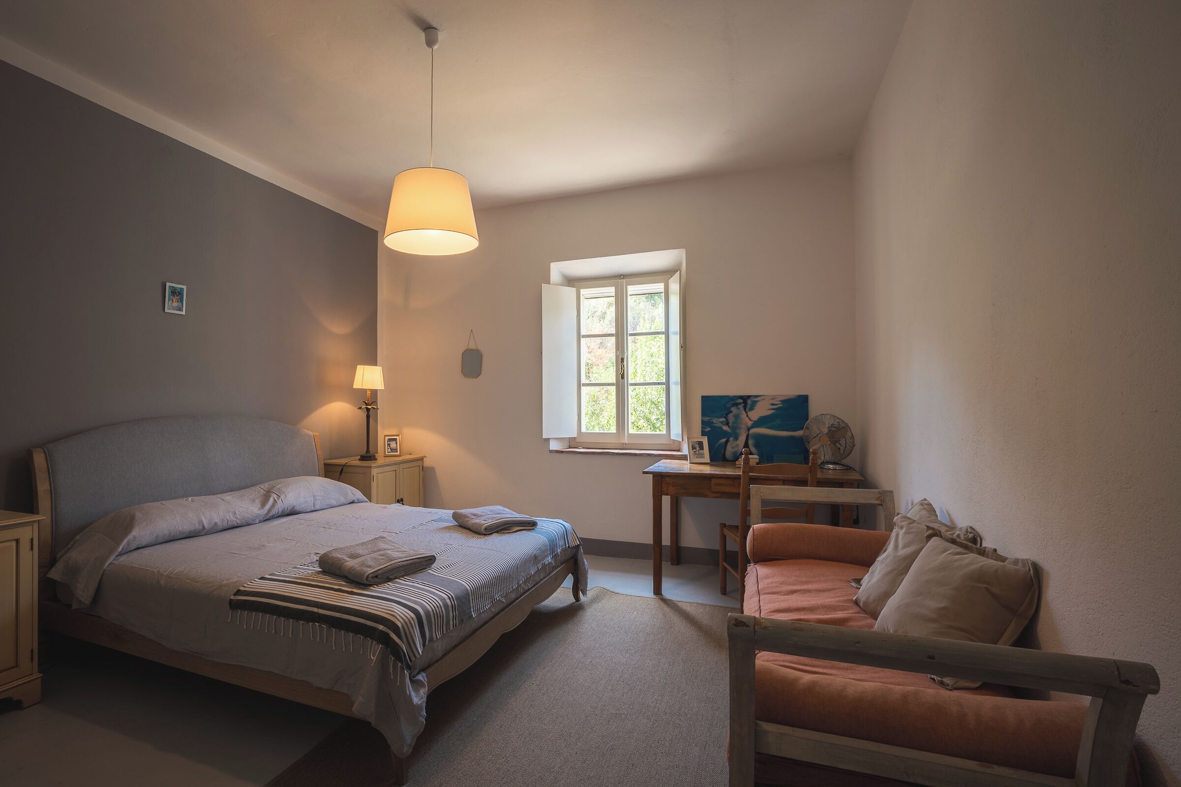A bedroom with a bed, a desk, a chair, a lamp, and a window.