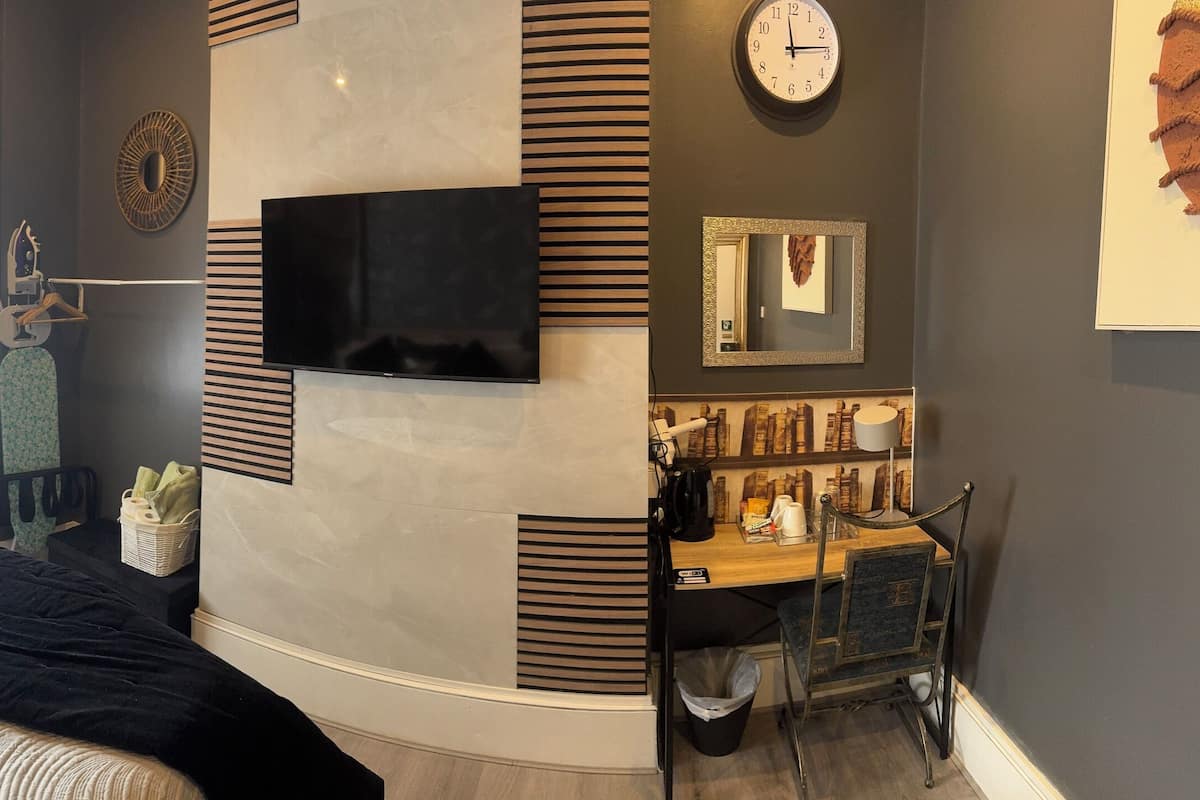 Une chambre à coucher moderne avec un lit, une télévision, une horloge et une petite table sur laquelle sont posés divers objets.