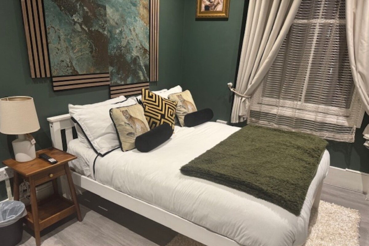 A bedroom with a bed, bedside table, lamp, and a painting on the wall.