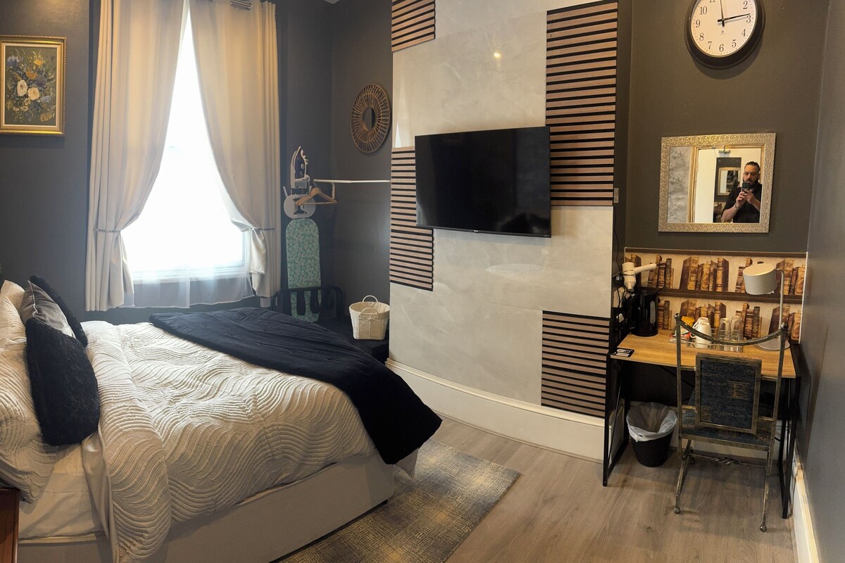 A modern bedroom with a bed, a TV, a clock, and a small desk area.