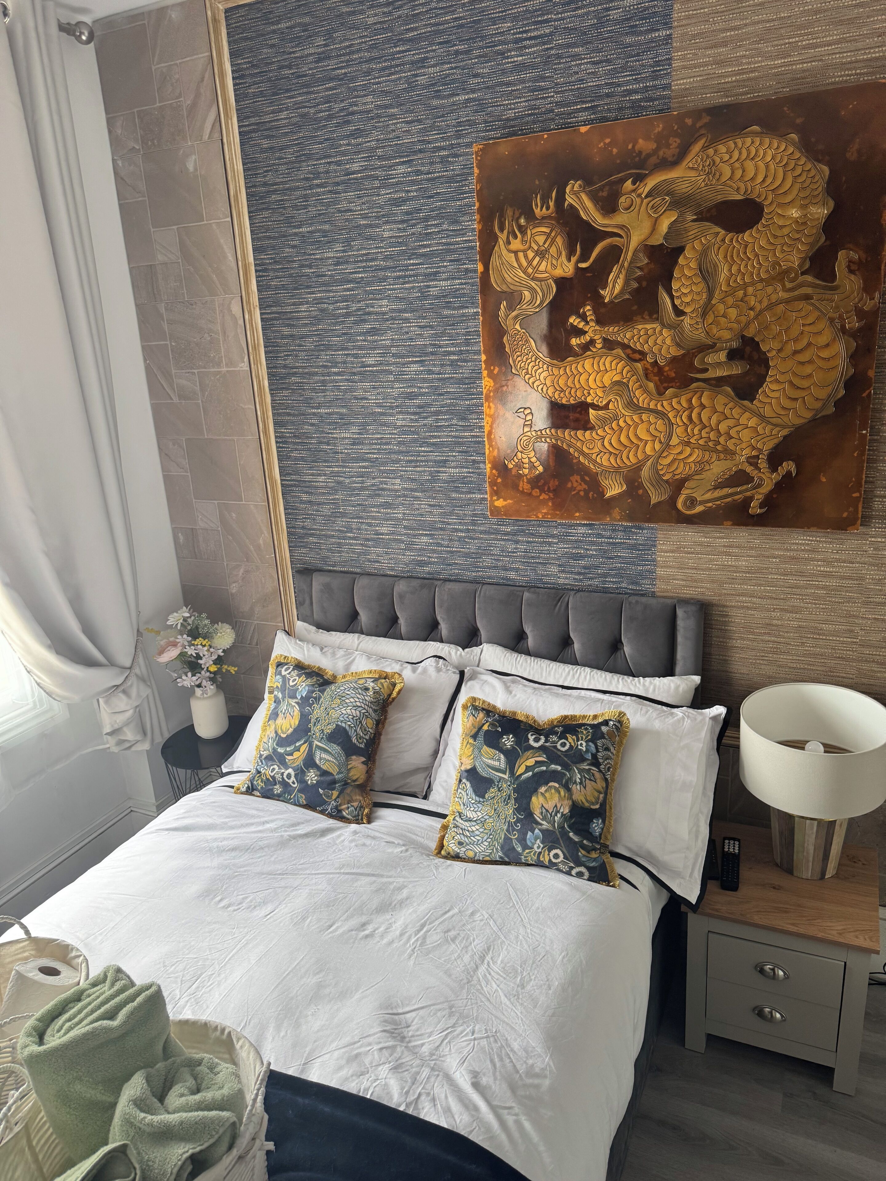 A bedroom with a bed, pillows, a nightstand, a lamp, and a decorative wall piece.