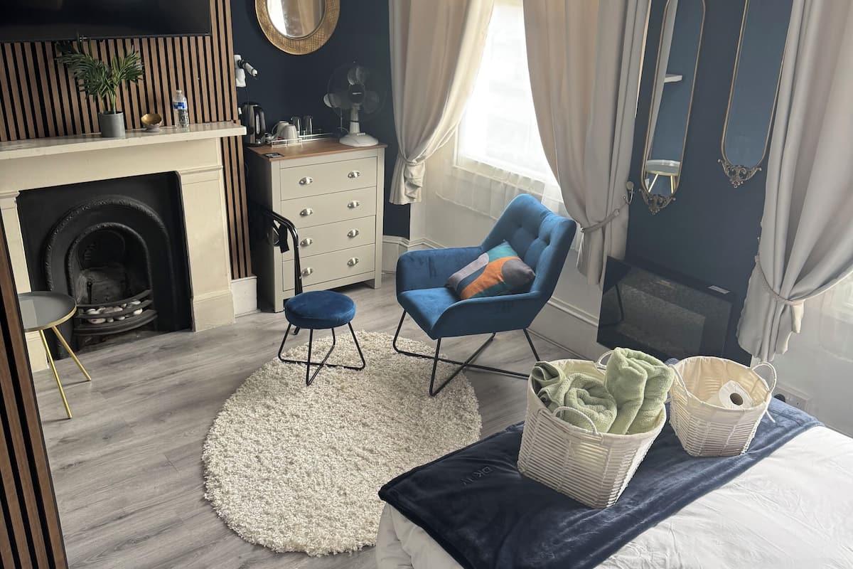 Une chambre moderne avec un lit, un fauteuil bleu, un tapis blanc et une cheminée.