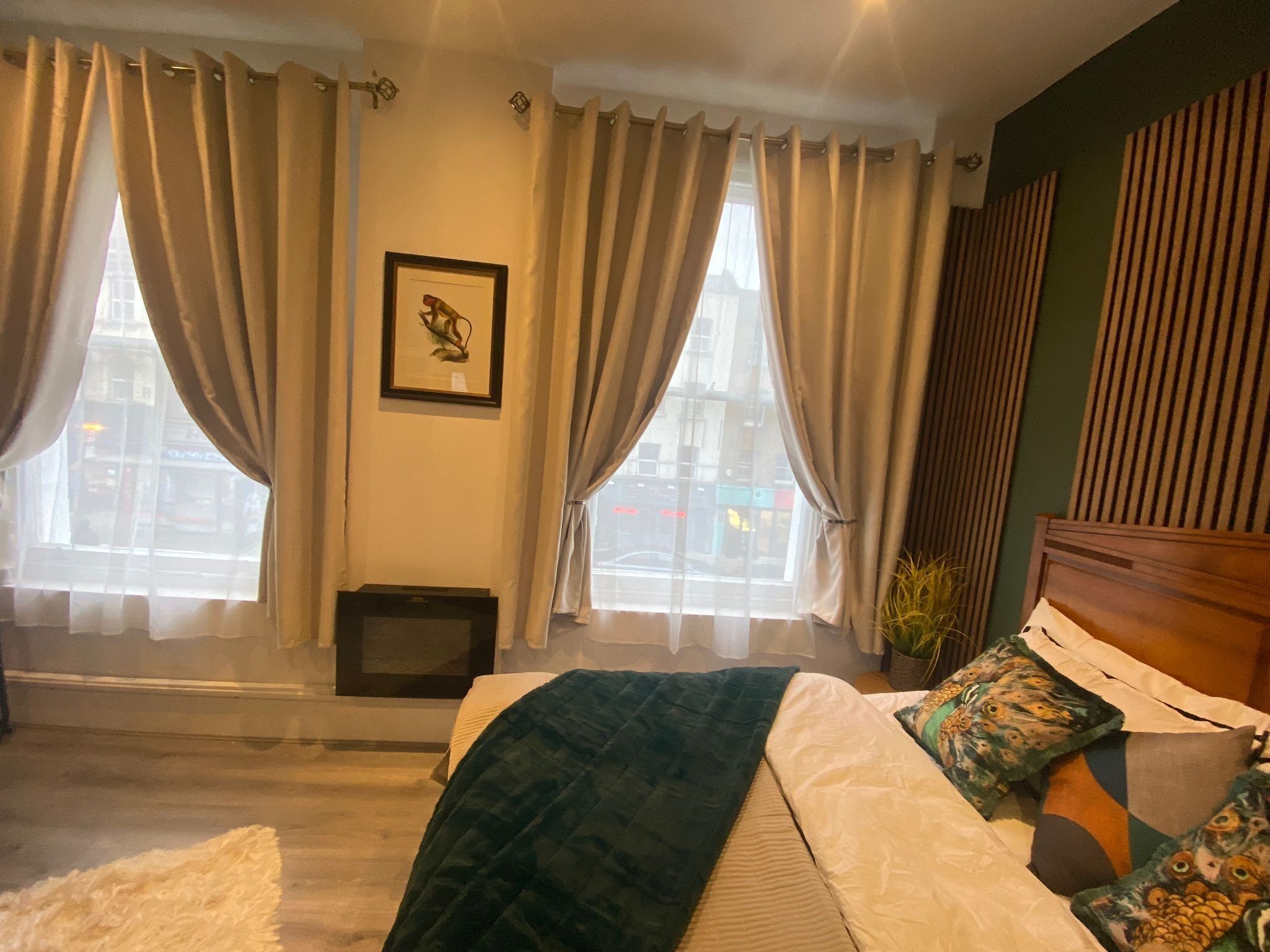 A bedroom with a bed, curtains, a picture on the wall, and a window with a view.