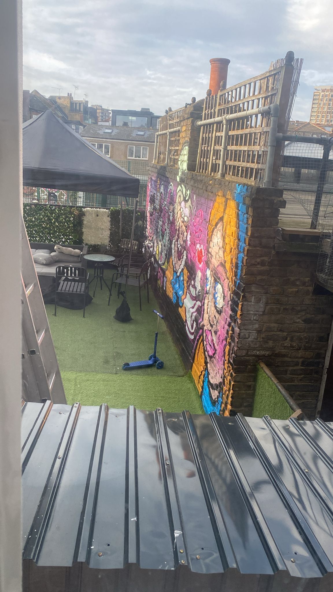 A rooftop terrace with a colorful mural, outdoor seating, and a view of the cityscape.