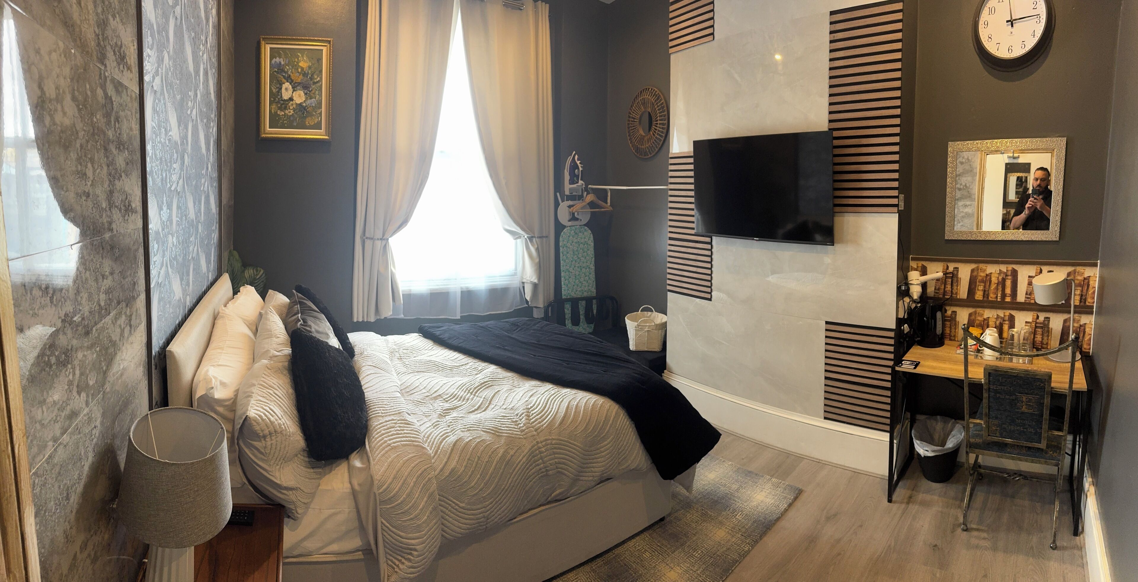A modern bedroom with a bed, a TV, a clock, and a small desk area.