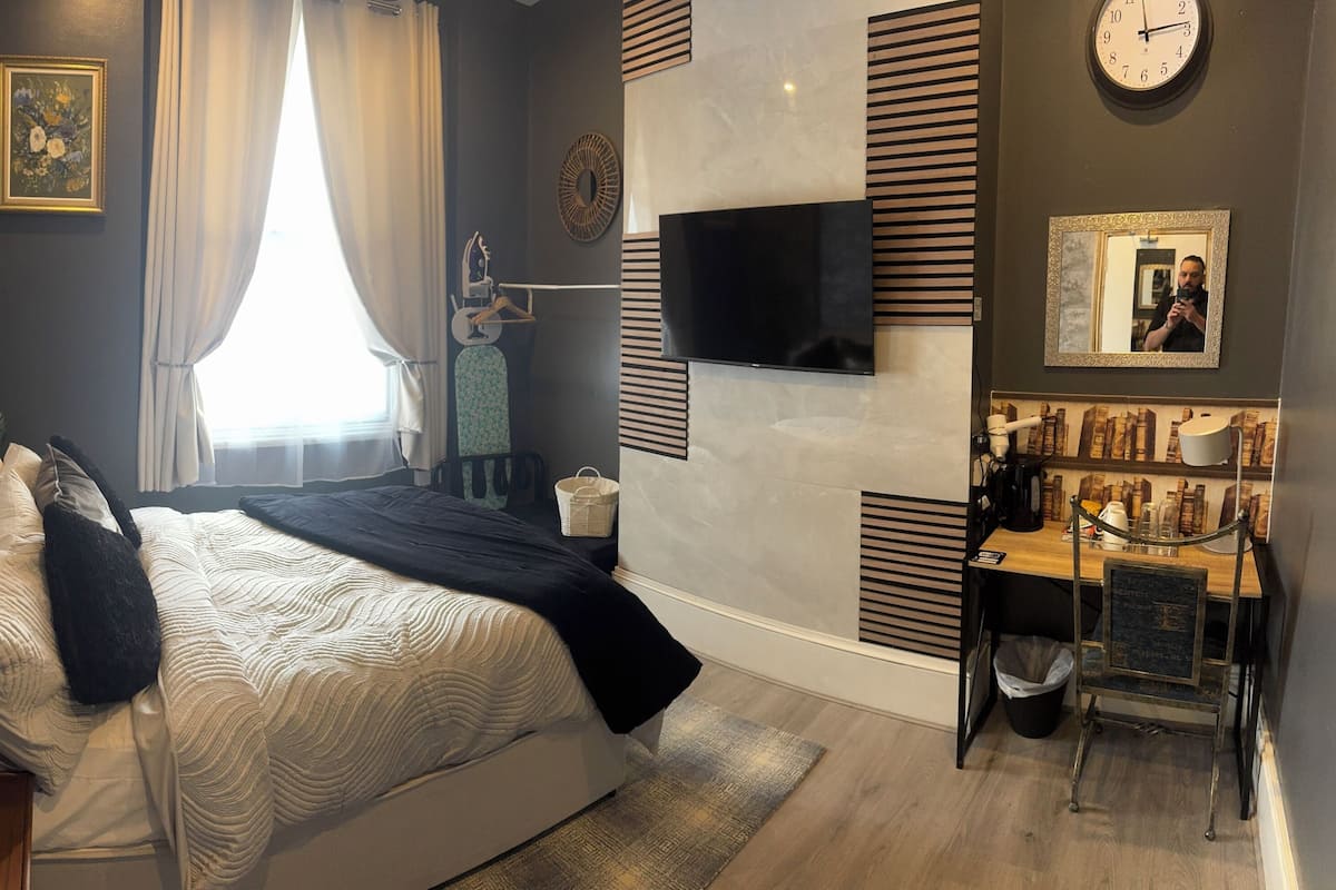 Une chambre à coucher moderne avec un lit, une télévision, une horloge et un petit bureau.