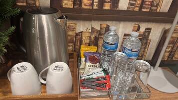 Un coin café équipé d’une bouilloire, de tasses et d’un plateau contenant des en-cas et des bouteilles d’eau.