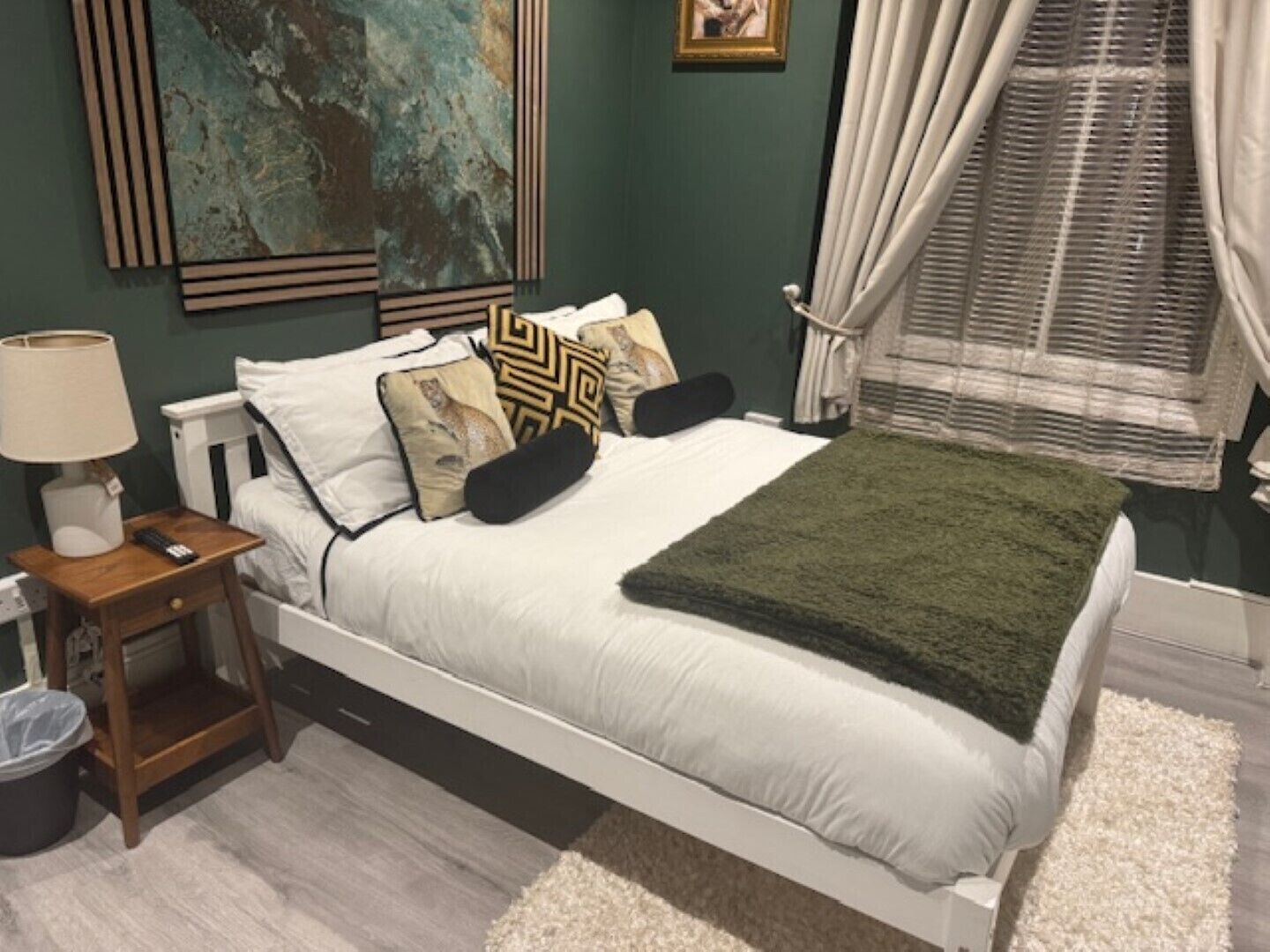 A bedroom with a bed, bedside table, lamp, and a painting on the wall.