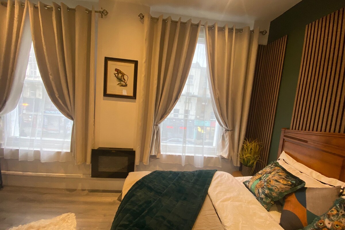A bedroom with a bed, curtains, a framed picture, and a window with a view of buildings.