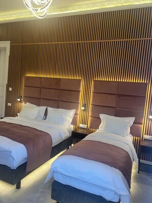 A hotel room with two beds, each with a headboard and bedside tables. The walls have a vertical wooden panel design, and there is a chandelier on the ceiling. - Bucharest Downtown Inn (Bucharest)
