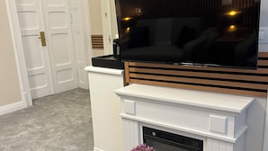 Un salón con televisor de pantalla plana sobre la chimenea, una puerta blanca y suelo alfombrado.