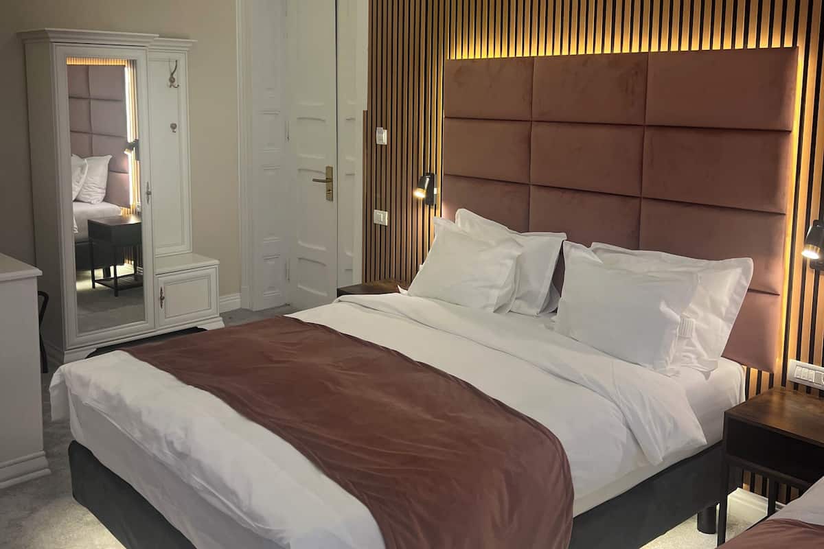Habitació d'hotel amb un llit gran, un armari, un mirall i una taula de nit amb una làmpada.