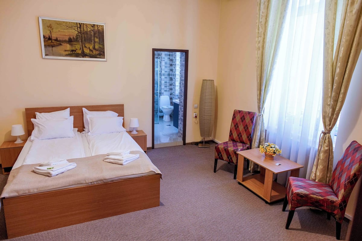Habitació d'hotel amb un llit gran, una taula petita amb un ram, dues cadires, una tauleta de nit i un quadre a la paret.