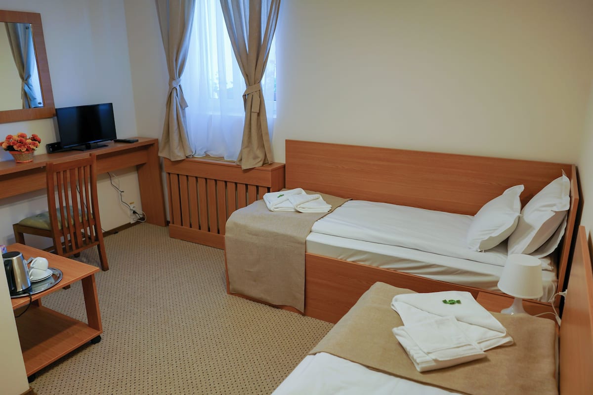 Habitació d'hotel amb escriptori de fusta, un llit, televisió i finestra amb cortines.